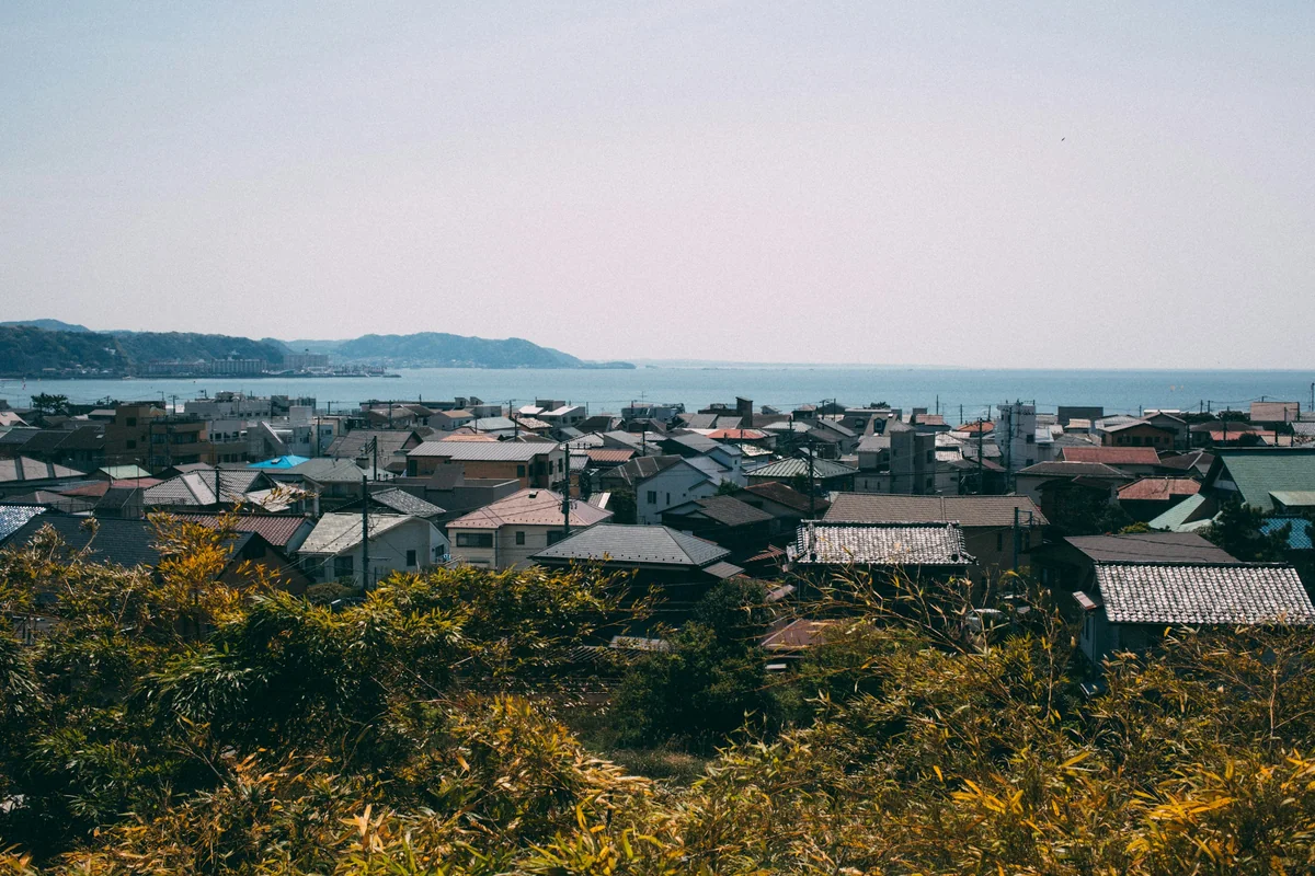 高台から見た海沿いの住宅地。低い屋根の家が並び、奥に海と山が見える